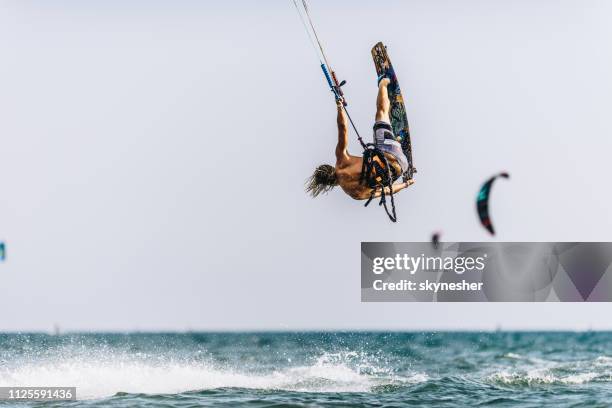 back view of a man kitesurfing in mid-air during summer day at sea. - adrenaline stock pictures, royalty-free photos & images