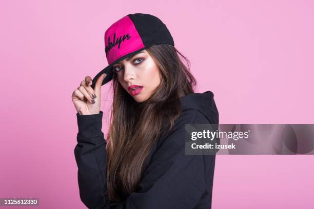 junge frau im schwarzen kapuzen shirt rosa hintergrund - female model stock-fotos und bilder