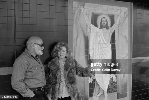 English director and actor John Schlesinger and American actress and singer Beverly D'Angelo near a painting of Jesus Christ, UK, 11th April 1980.