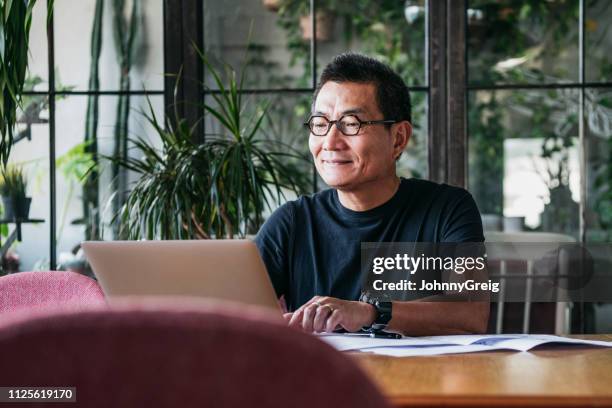sonriente hombre chino trabajando en ordenador portátil en casa - mature chinese man fotografías e imágenes de stock