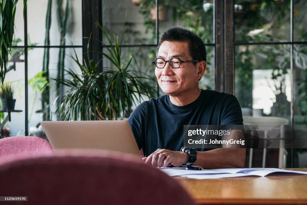 Smiling Chinese man working on laptop at home