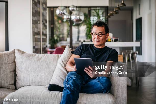 homme d’âge mûr portant des lunettes à l’aide de tablette numérique - adulte dâge mûr photos et images de collection