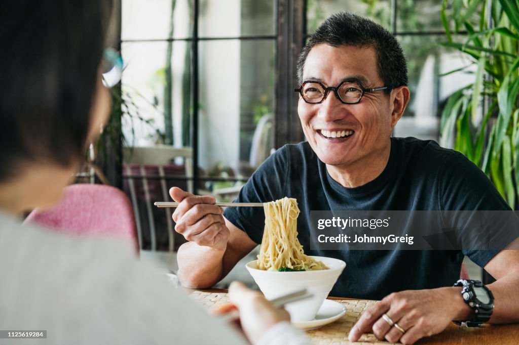 Mature man eating bowl of noodles and laughing