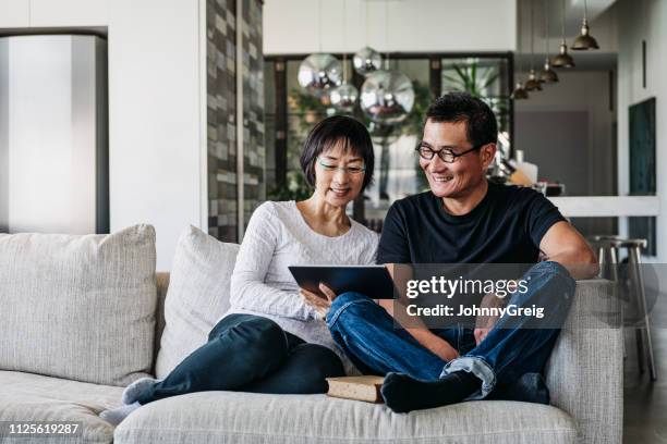 chinese couple on sofa watching movie online - comfortable retirement stock pictures, royalty-free photos & images