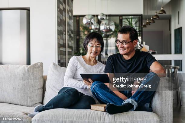 chinese couple on sofa watching movie online - asian couple imagens e fotografias de stock