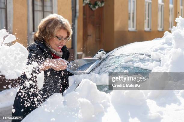 ältere frau, die reinigung des schnee von einem auto - city cleaning stock-fotos und bilder