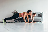 Two fitness women doing push-ups exercise working out at home. Side view