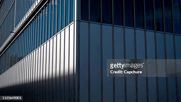 windows of a corporate downtown city office building reflect the sky and surroundings as the sun cuts a shadow line across the facade. - schweiz stadt stock-fotos und bilder