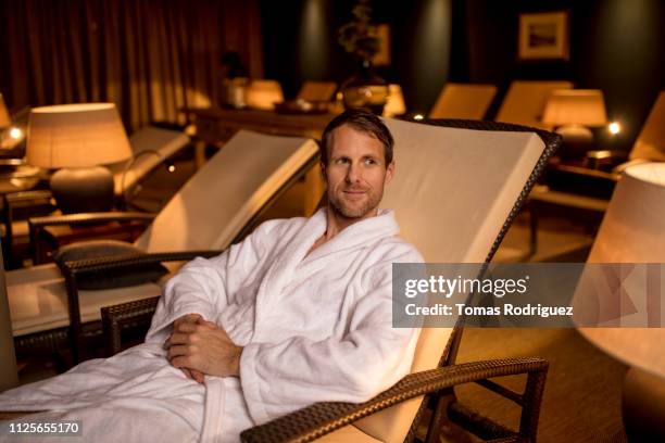 man in bathrobe resting in lounge chair in relaxation room of a spa - balneario fotografías e imágenes de stock