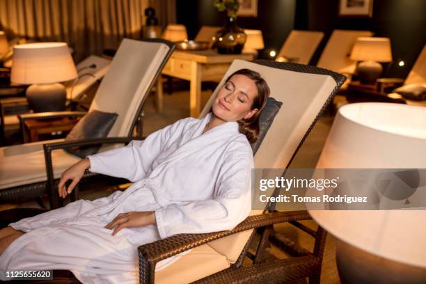 young woman in bathrobe resting in lounge chair in relaxation room of a spa - balneario fotografías e imágenes de stock