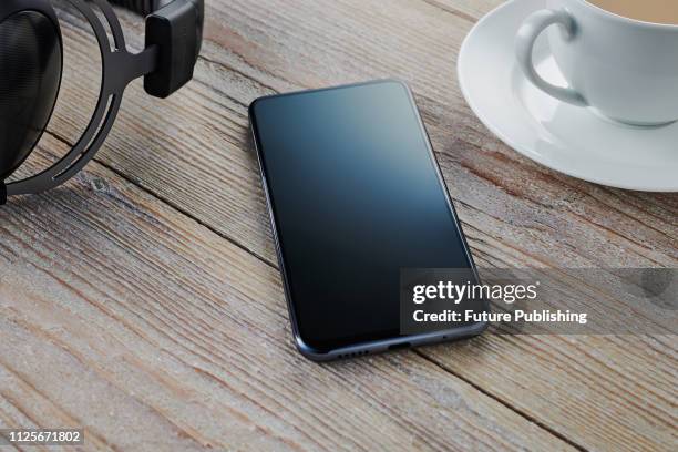 An Android smartphone with a blank screen alongside a cup of tea and a pair of over-ear headphones, taken on February 7, 2019.