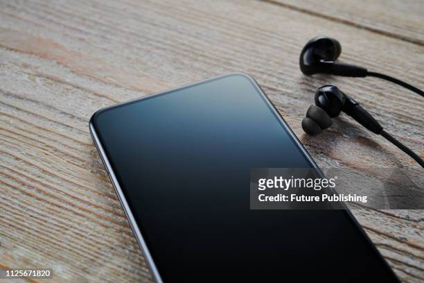 An Android smartphone with a blank screen alongside a pair of earphones, taken on February 7, 2019.