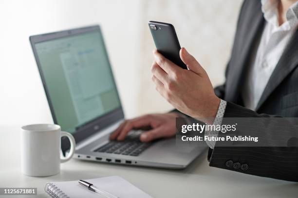 Close up detail of a businessman working at a desk with a smartphone and laptop computer, taken on January 31, 2019.