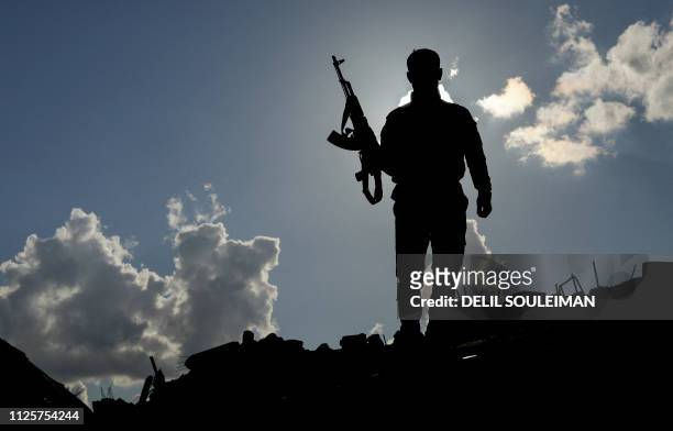 Fighter of the US-backed Syrian Democratic Forces stands guard in the frontline Syrian village of Baghouz on February 18, 2018. - SDF forces have...