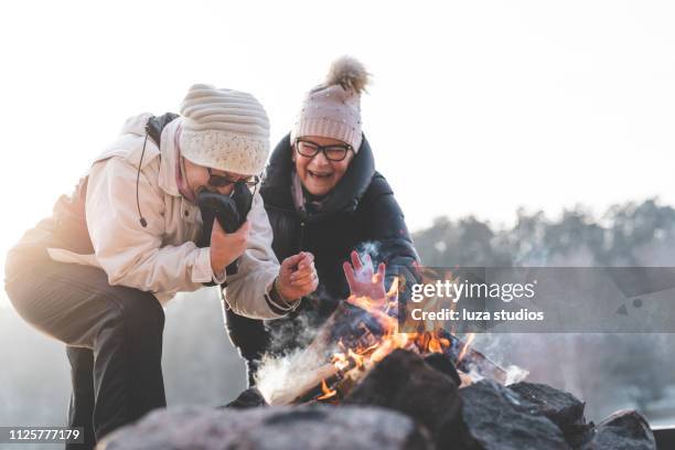two senior women by a campfire in winter - campfire stock pictures, royalty-free photos & images