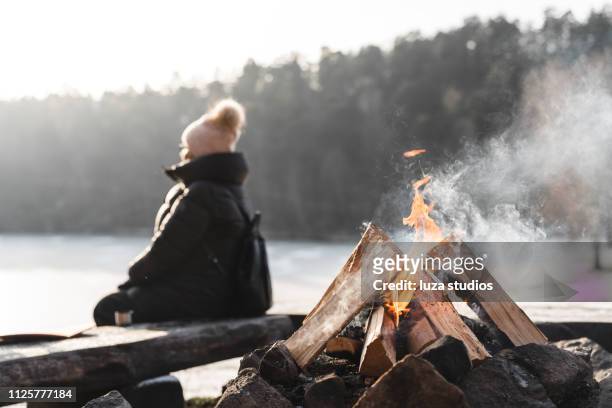 een senior vrouw door een kampvuur in de winter - middle aged woman winter stockfoto's en -beelden