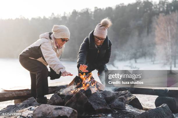 twee senior vrouwen door een kampvuur in de winter - bukken stockfoto's en -beelden