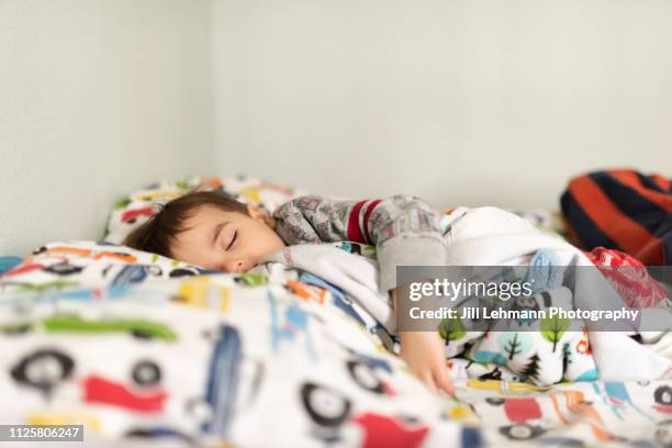 toddler is sleeping on a bed attempting to recover from the cold and flu season. - sleeping toddler bed stock-fotos und bilder