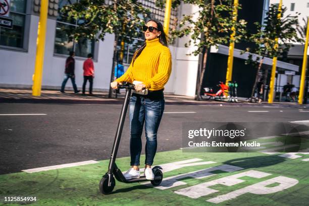 a woman driving an electric scooter on a scooter & bike lane in the city downtown - trotinete imagens e fotografias de stock