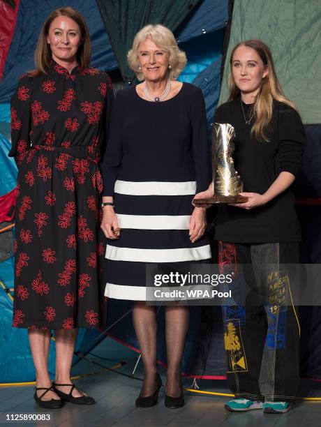 Camilla, Duchess Of Cornwall stands with Caroline Rush Chief Executive of The British fashion Council and designer Bethany Williams who was awarded...