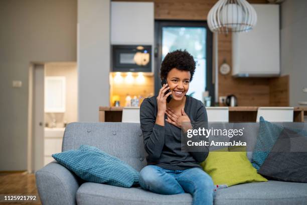 young african american woman einen anruf tätigen und auf dem sofa sitzen - erleichterung stock-fotos und bilder