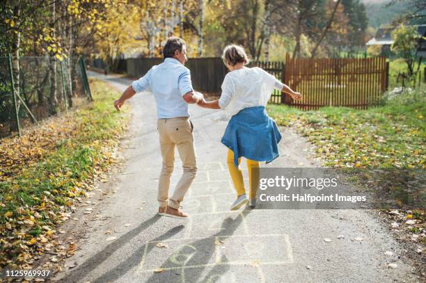 a rear view of senior couple jumping on a road outdoors, playing hopscotch. - hopscotch stock-fotos und bilder