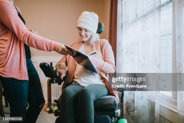 cheerful young woman in wheelchair at home signing papers - cerebral palsy stock pictures, royalty-free photos & images