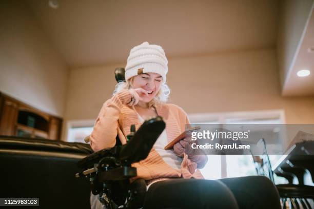 cheerful woman in wheelchair on smartphone at home - orthopaedic equipment imagens e fotografias de stock