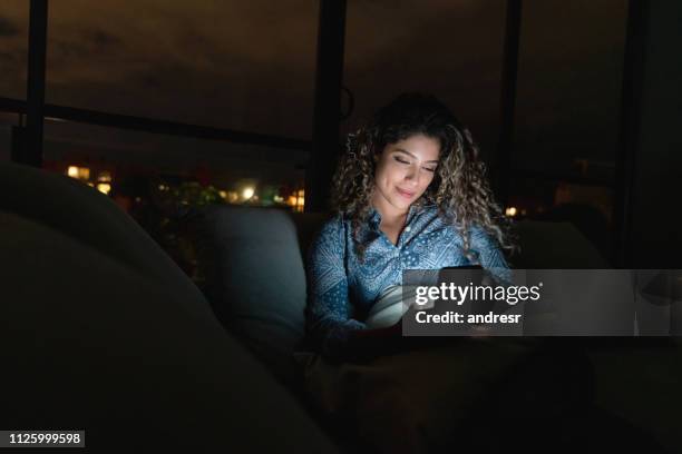 woman at home using app on her cell phone while relaxing at nighttime - dark cells stock pictures, royalty-free photos & images