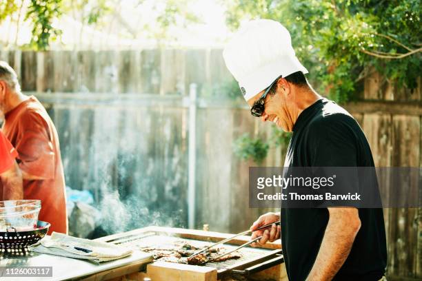 smiling father grilling in backyard during family barbecue - bbq father stock-fotos und bilder