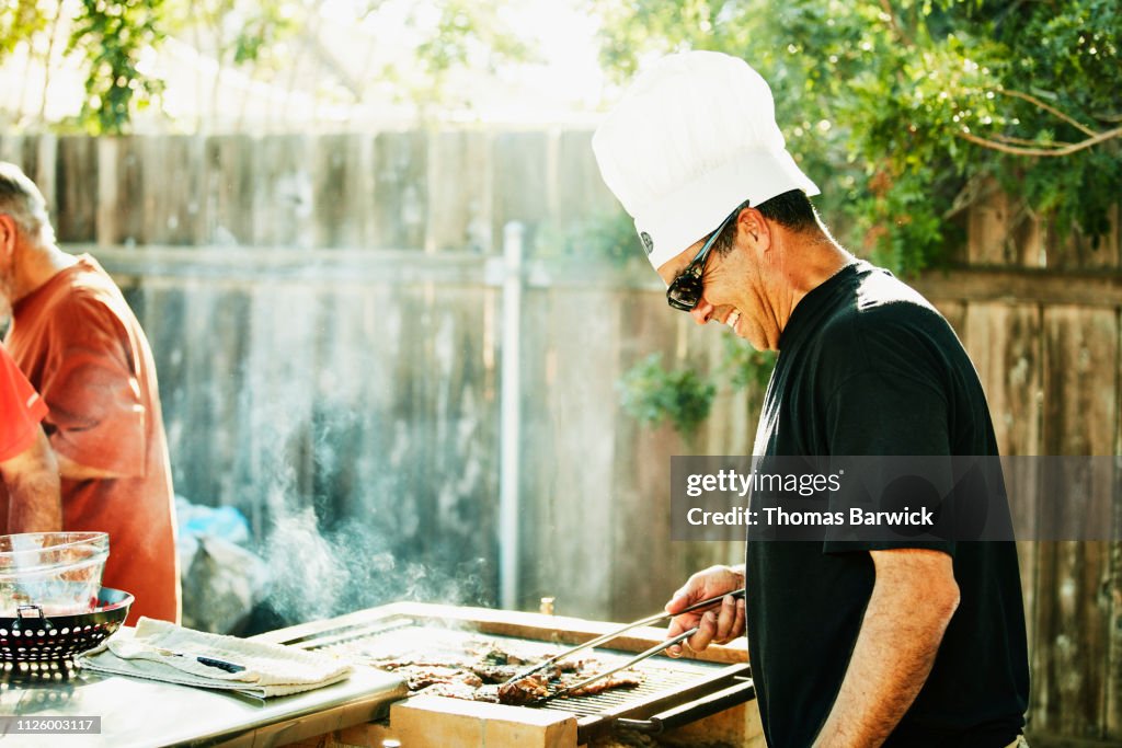 Smiling father grilling in backyard during family barbecue