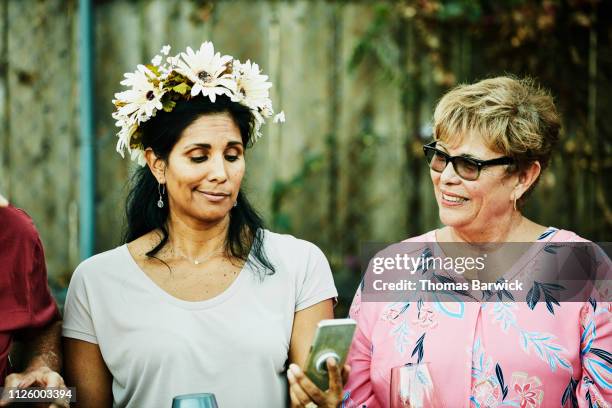 woman making a face while looking at smart phone during backyard family barbecue - bloemkroon stockfoto's en -beelden