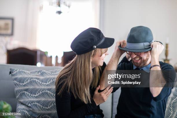 millennial couple sitting on the sofa wearing hats - bowler hats stock pictures, royalty-free photos & images