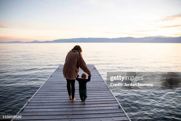 a mom teaching her young son to walk on a dock. - primi passi foto e immagini stock