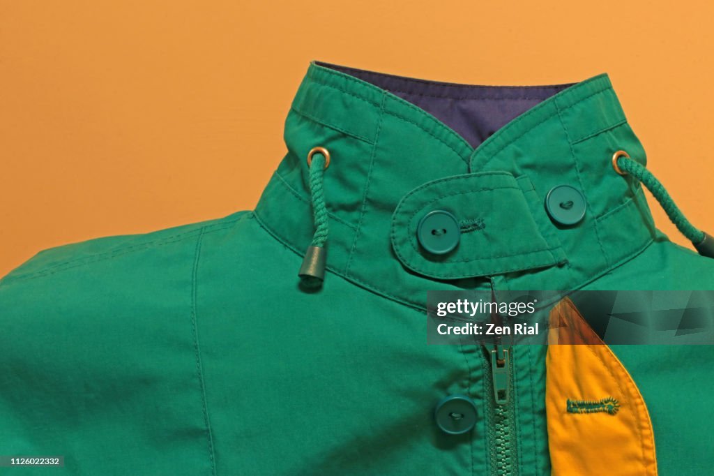 Green jacket against yellow background showing buttoned up collar, zipper and lining