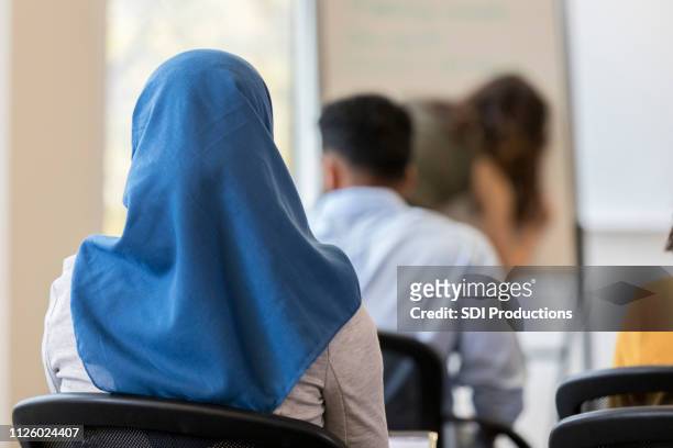 vista posterior de la mujer con hijab sentada en el salón de clases - islamismo fotografías e imágenes de stock