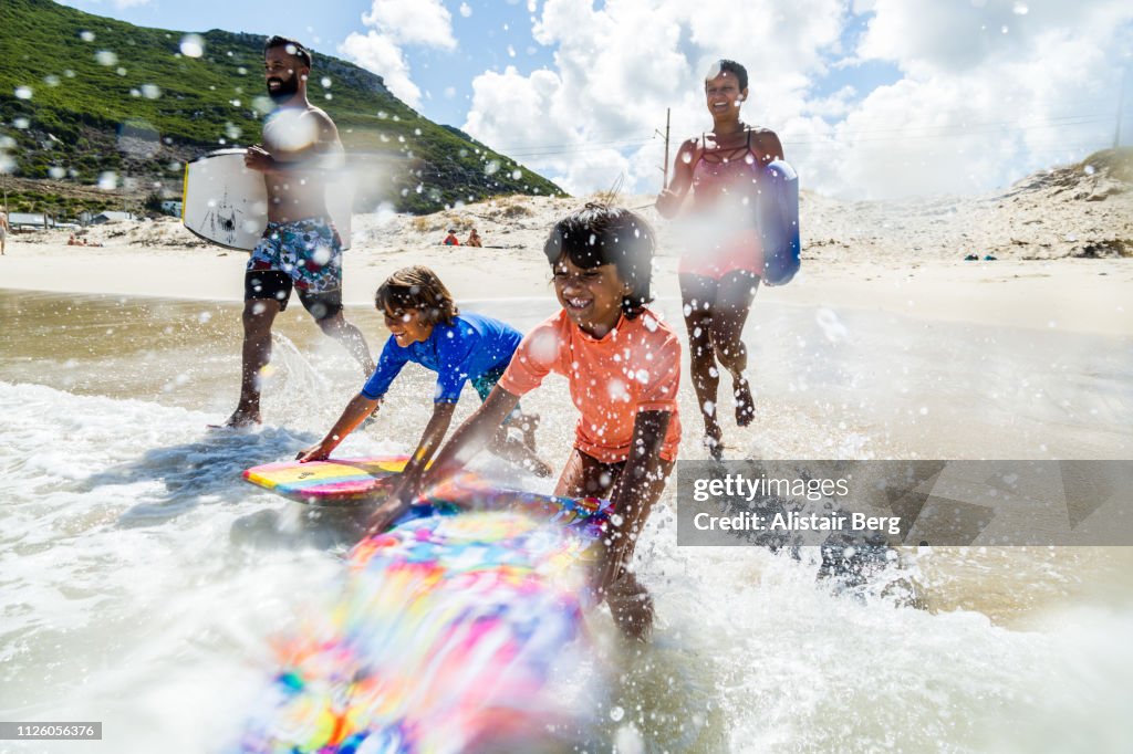 Family running and splashing into sea together with body boards