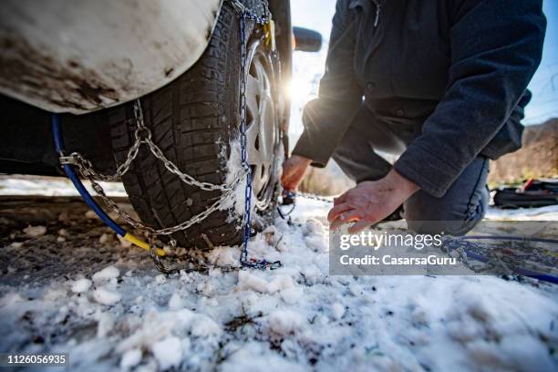 adult man positioning tire chains on a car - tyre chain stock pictures, royalty-free photos & images