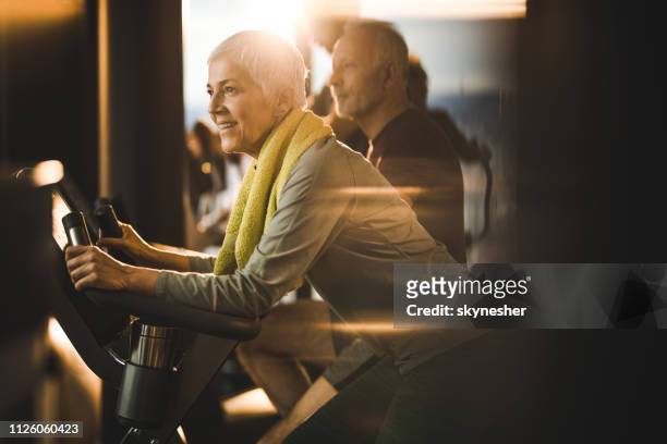 happy senior woman on a exercising class in a gym. - spin class stock pictures, royalty-free photos & images