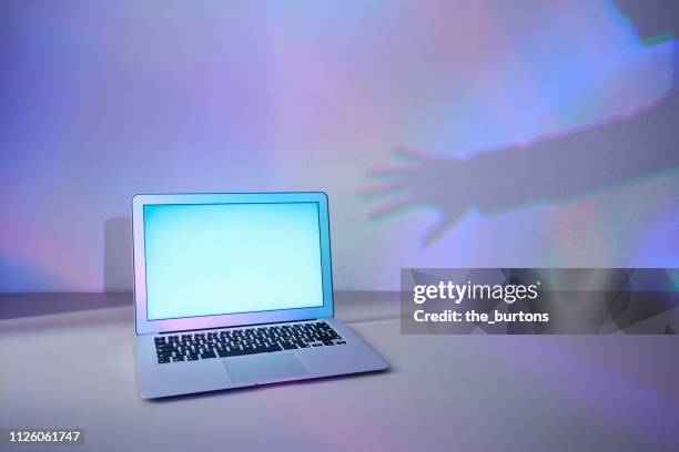 laptop and shadow of a hand, conceptual image of data theft and cyber crime - cyberbullying fotografías e imágenes de stock