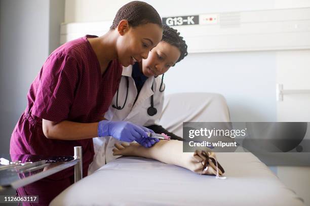 mujeres estudiantes de medicina práctica de costuras en una jeringa de prótesis de brazo de práctica - sutura fotografías e imágenes de stock