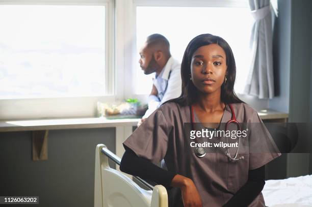 female doctor sitting on bed with male doctor behind staring out of the window - inequality stock pictures, royalty-free photos & images