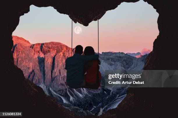 couple on swing contemplating the mountains in a romantic view with heart shape. - valentines day holiday stock-fotos und bilder