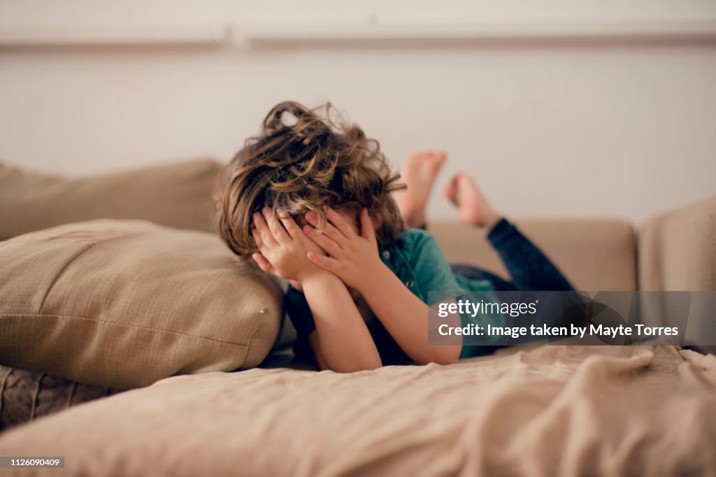 Toddler laying in sofa covering his face
