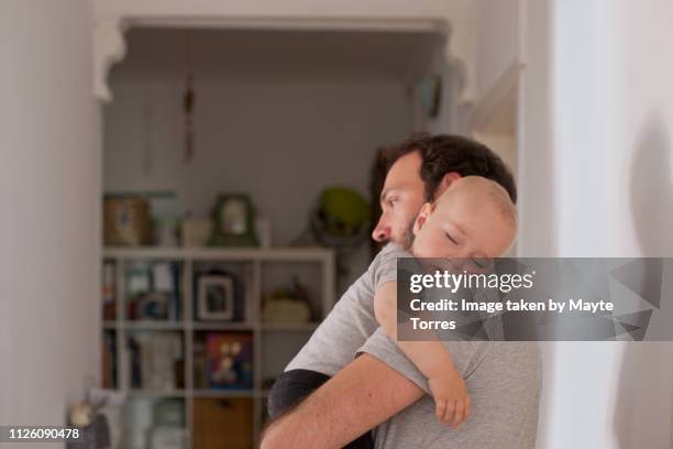 dad putting to sleep baby boy in his arms - neue männlichkeit stock-fotos und bilder
