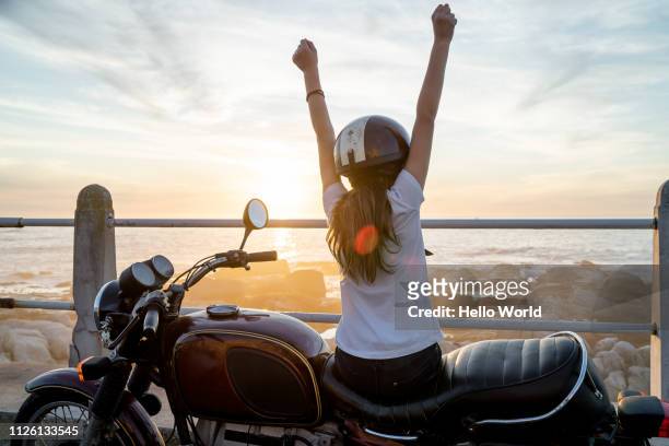 young girl sitting on retro motorcycle showing victory with arms - mare moto foto e immagini stock