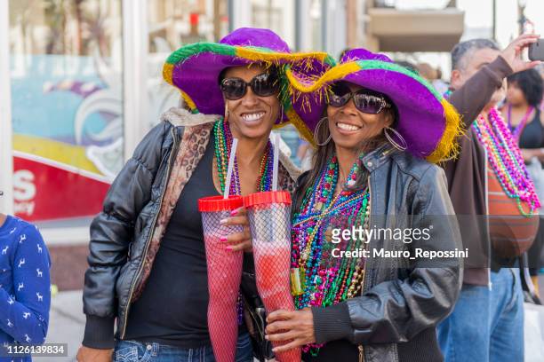 twee vrouwen glimlachend met hun drankjes dragen hoeden in de straat tijdens de viering van de mardi gras in new orleans carnaval, louisiana, verenigde staten. - mardi gras fun in new orleans stockfoto's en -beelden