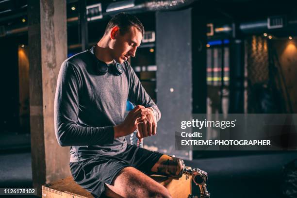 junge männliche athlet mit einer beinprothese setzen eine fitness-tracker-uhr und immer bereit, in einer holzkiste in einem crossfit gym trainieren - zeitumstellung stock-fotos und bilder