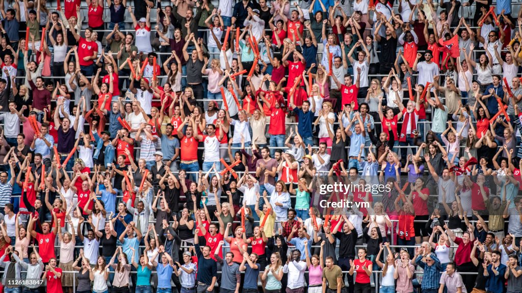 Sports fans in red jerseys cheering on stadium bleachers