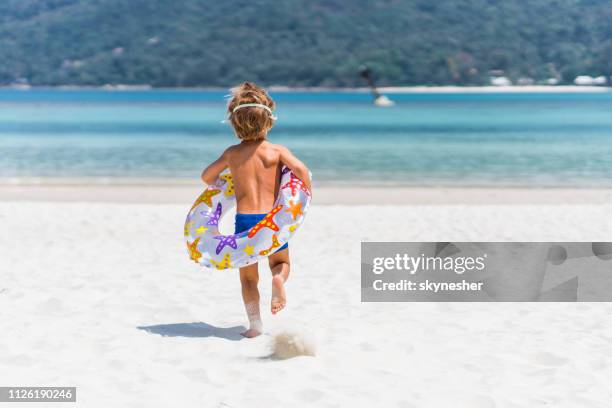 vista posteriore del bambino spensierato che corre con tubo di nuoto verso il mare. - salvagente foto e immagini stock